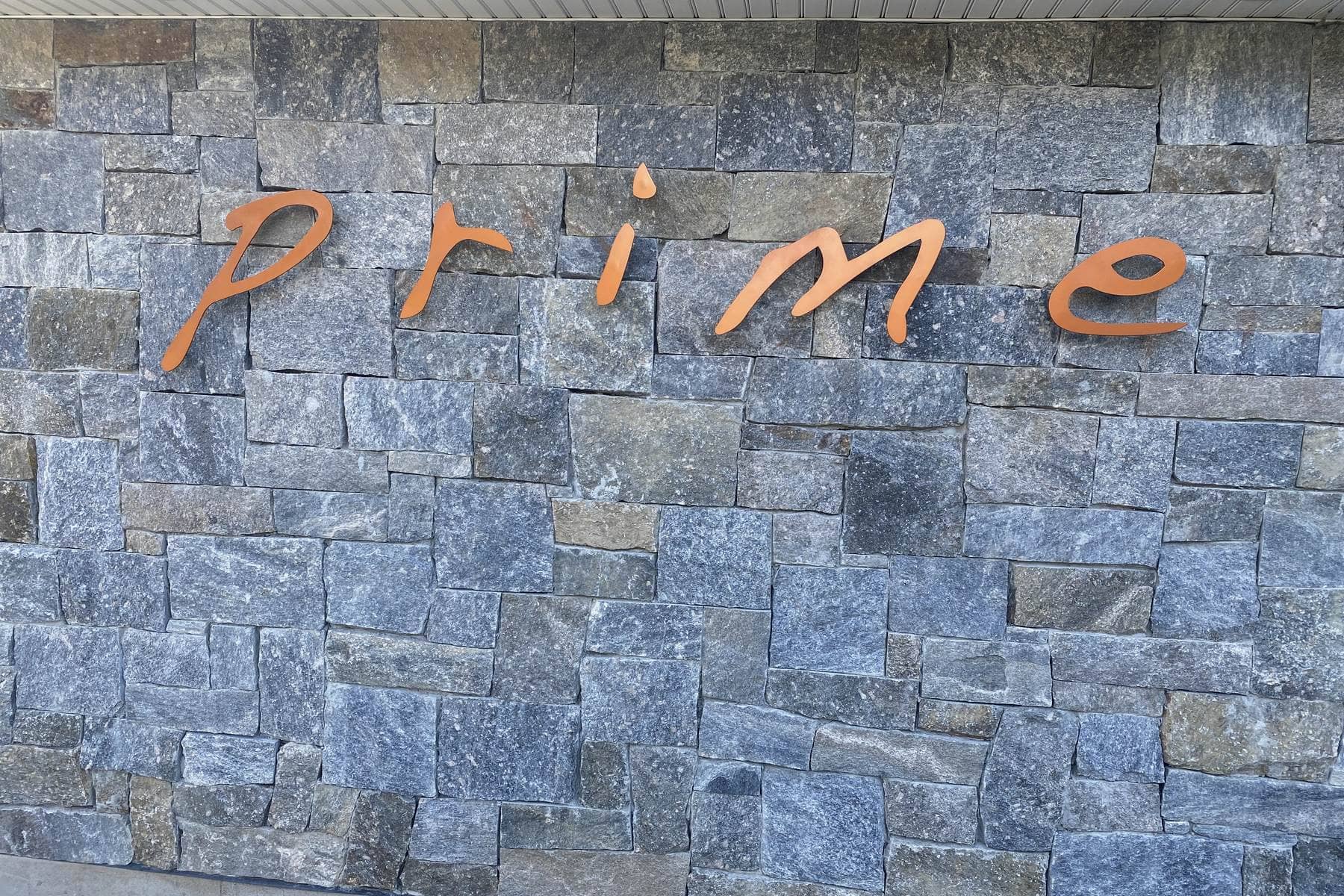 Taino Prime stainless script signage on a stone wall